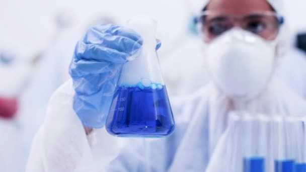 Científica en un laboratorio recogiendo y sosteniendo un líquido azul humeante en una botella — Vídeos de Stock