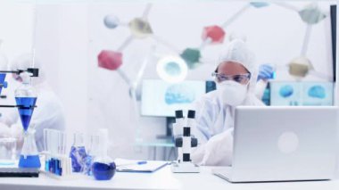 Laboratuvarda mikroskoptan bakan kadın bilim adamı koruma ekipmanı takıyor