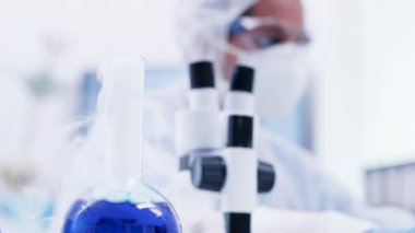 Laboratuvar şişesinde sigara içen mavi sıvıve dizüstü bilgisayarda yazan bilim adamının yakın çekim