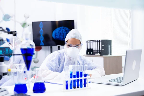 여성 화학자가 파란색 액체가 있는 튜브 홀더를 봅니다. — 스톡 사진