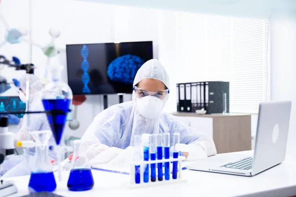 A química feminina olha para um suporte de tubo com um líquido azul — Fotografia de Stock