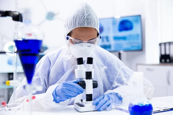 Chemist with safety glasses looks in the microscope and adjusts it — Stock Photo, Image