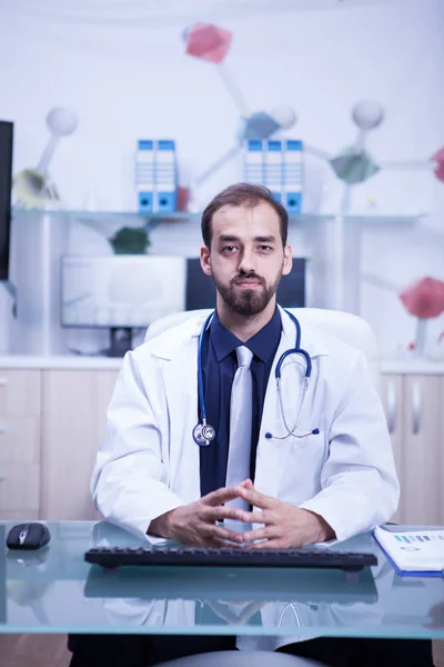 Молодой и интеллигентный доктор в своем кабинете в белом халате и стетоскопе — стоковое фото