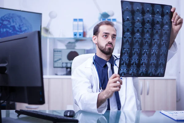 Guapo médico neurológico mirando una tomografía computarizada cerebral en el gabinete — Foto de Stock