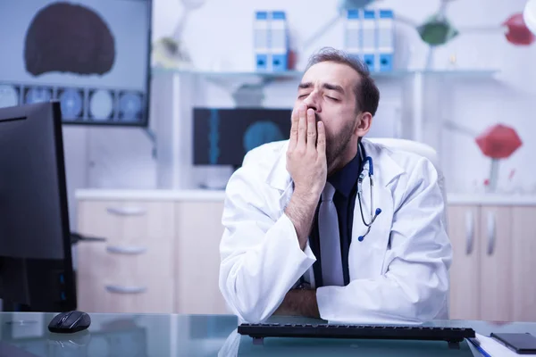 Mladý vousatý doktor unavený a zíval v kanceláři v nemocničním kabinetu — Stock fotografie
