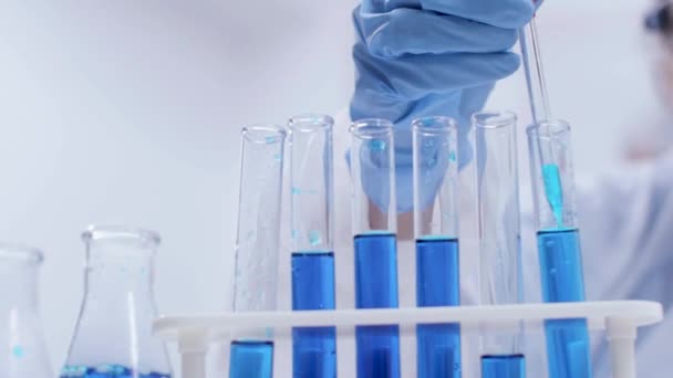 Test tüplerinden mavi sıvı ile bilimsel test yapan kadın bilim adamının el görüntülerine yakın — Stok video