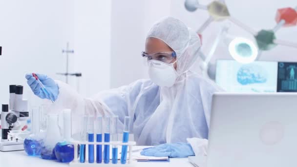 Scienziata focalizzata donna in tuta protettiva attrezzature facendo test scientifici con fumo liquido blu — Video Stock