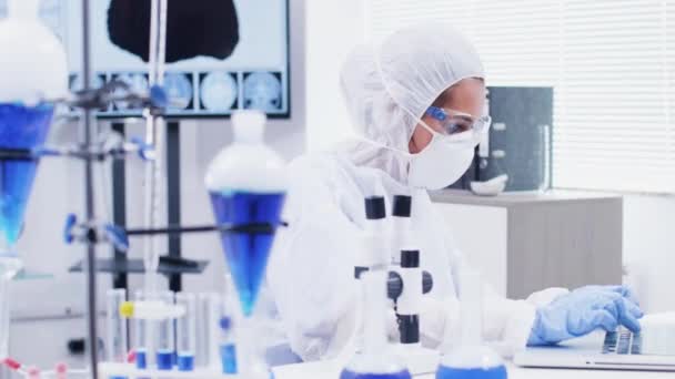 Científica femenina escribiendo fórmula en el portátil y mirando a través del microscopio en el laboratorio de ciencia moderna — Vídeo de stock
