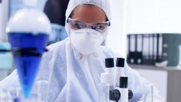 Cientista feminina em equipamento de macacão segurando e olhando para tubo est com líquido azul — Vídeo de Stock