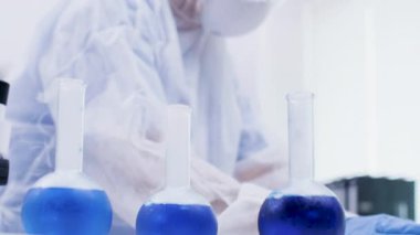 Kadın bilim adamı tutma ve araştırma laboratuvarında reaktif ile mavi bir çözüm bakıyor