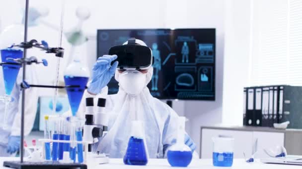 Young female scientist in chemistry lab with virtual reality headset zooming out — Stock Video