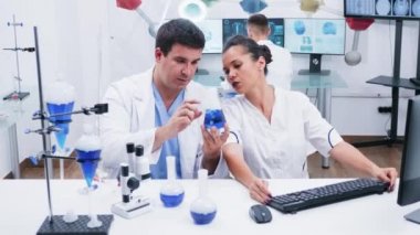 Beyaz önlüklü genç kadın bilim adamı modern bir araştırma laboratuvarında asistanıyla çalışıyor