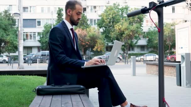 Junger Manager im Anzug arbeitet draußen in der Stadt am Laptop — Stockvideo