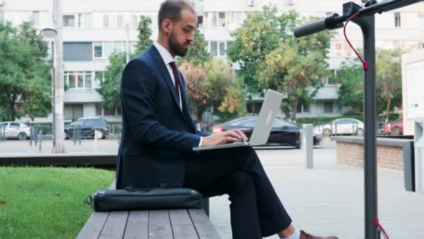 Mann im Businessanzug tippt auf dem Laptop vor seinem Büro in der Stadt — Stockvideo