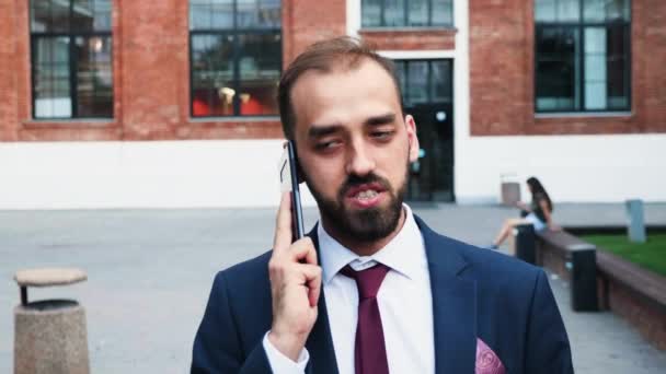 Businessman in suit walking and talking on the phone in front of the business district — Stock Video