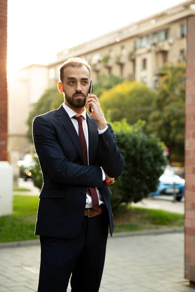 Jovem empresário vestido de terno fala no celular na rua — Fotografia de Stock