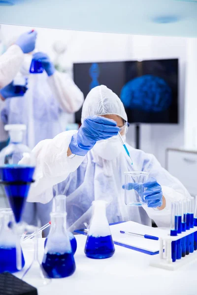 Scheikundige druipend van de pipet een blauwe vloeistof in een container — Stockfoto