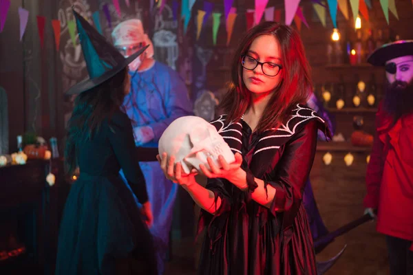 Menina com óculos vestidos como bruxa olhando para o crânio humano — Fotografia de Stock