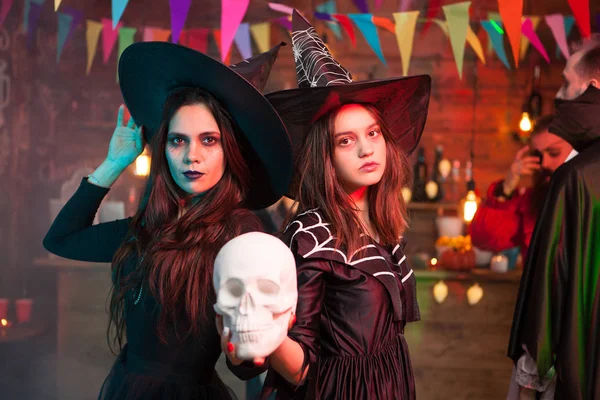 Duas meninas bonitas em vestidos pretos e chapéus de bruxas segurar um crânio para festa de Halloween — Fotografia de Stock