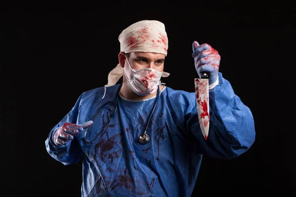 Enge dokter met kwade gezicht kijken naar zijn mes in Studio — Stockfoto