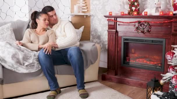 Красивая пара, лежащая вместе в кровати, глядя на камин в украшенной рождественским убранством комнате — стоковое видео