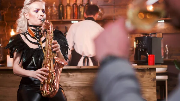 Blonde woman in a jazz club singing jazz music on her saxophone