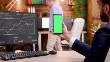 Yeşil ekranlı bir telefon tutan işadamının arka görünümü