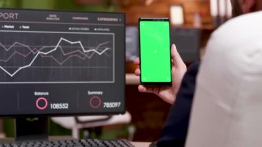 Yeşil ekranlı cep telefonu tutan beyaz işadamının arka görünümü.