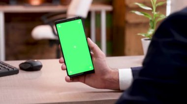 Yeşil ekranlı cep telefonu tutan ofisinde işadamının arka görünümü