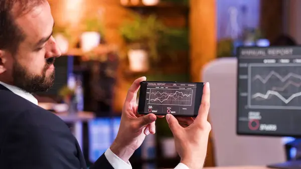 Крупным планом бизнесмен смотрит на графику на экране смартфона — стоковое фото