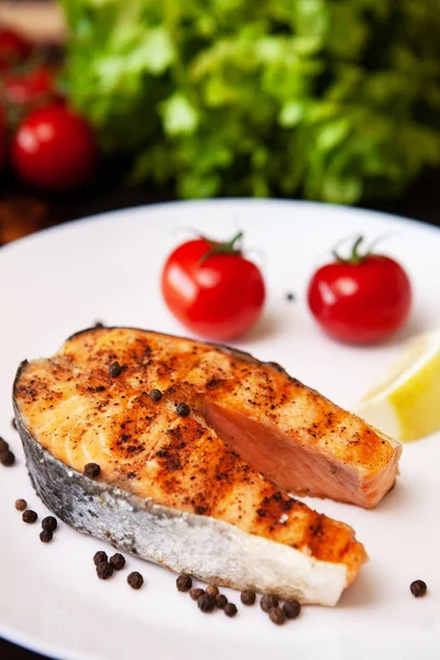 Salmón cocido en la parrilla dispuesto en un plato con tomates y pimienta negra — Foto de Stock
