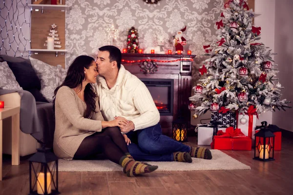 Young husband kissing his wife forehead on christmas day in front of their warm fireplace — Stock Photo, Image