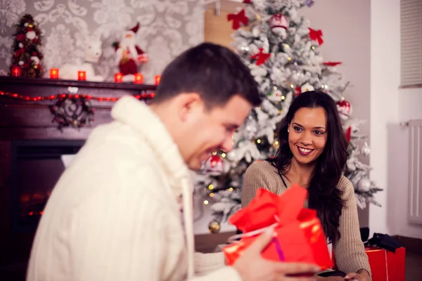 Bonita joven esposa mirando con entuziasm a su marido mientras él abre el presente —  Fotos de Stock