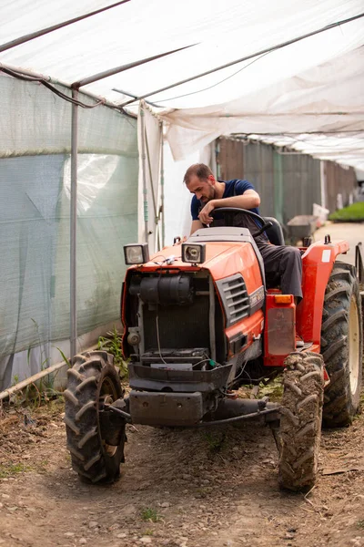 Jonge boer probeert een tractor te starten in een kas — Stockfoto