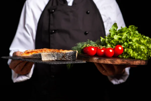Chef sosteniendo dos encimeras una con salmón frito y la otra con tomates y ensalada — Foto de Stock