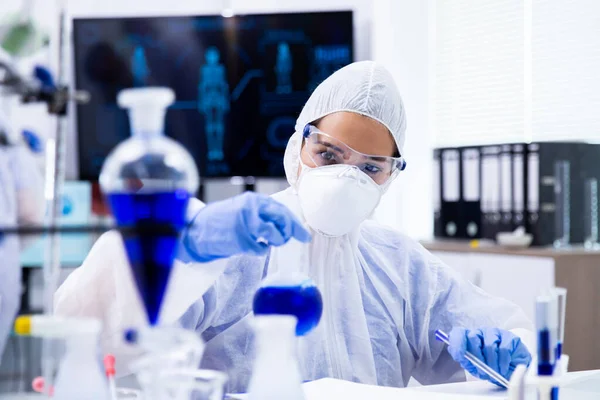 Investigador mezclando un líquido azul en un tubo y mirándolo —  Fotos de Stock