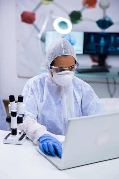 Scienziata focalizzata che indossa attrezzature di protezione lavorando sul suo computer portatile — Foto Stock