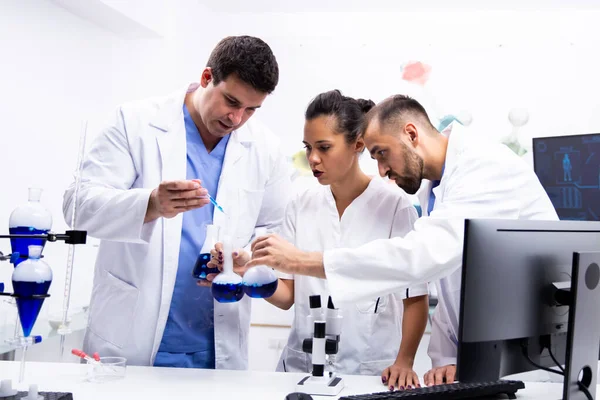 Equipo de científicos en bata blanca trabajando junto con el líquido azul humeante —  Fotos de Stock