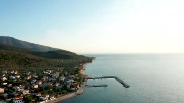 Deniz üzerinde turkuaz su ve kıyı şeridi yakınlarındaki evlerle uçan insansız hava aracı.