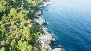 İnsansız hava aracı turkuaz deniz suyuyla kayalık sahil şeridinde uçuyor.
