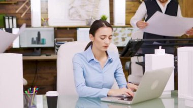 Genç bayan mimar dizüstü bilgisayarda çalışıyor ve baş inşaatçıyla konuşuyor.