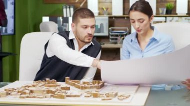 Mimarlardan oluşan bir ekip mavi baskı tutuyor ve modellerle çalışıyor.