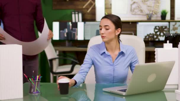 Vrouwelijke hoofdarchitect neemt een slokje koffie en helpt haar collega — Stockvideo