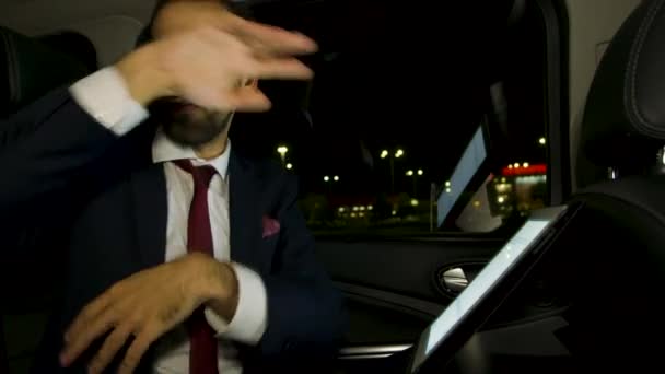 Серьезный бизнесмен, работающий над планшетом ночью на заднем сиденье своего лимузина с личным водителем — стоковое видео