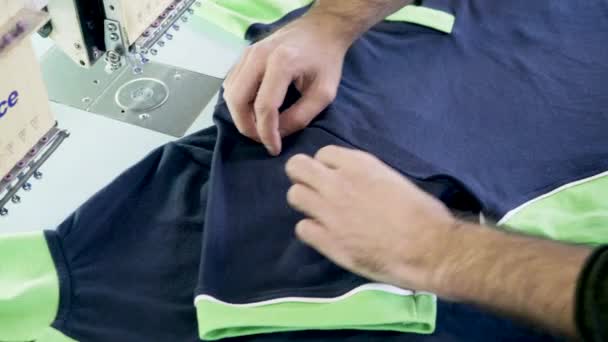 Muž v šicí továrně kontroluje šití trička — Stock video