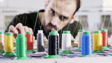 Kumaş fabrikasındaki adam dikiş ipliğini kontrol ediyor.