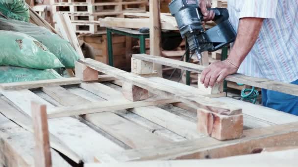 Man in een warenhuis met een spijkerpistool voor houten pallets — Stockvideo