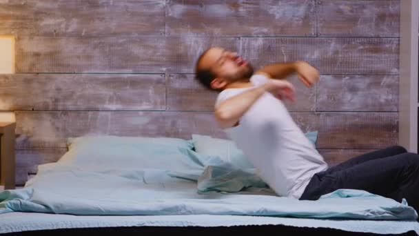 Young caucasian man yawning and falling on his back in the bed — Stock Video