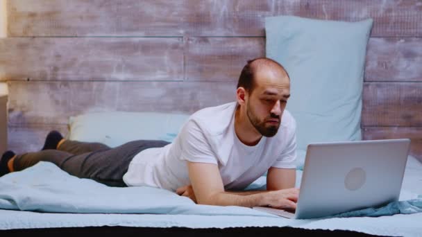 Young adult lying in his bed working on laptop late at night — Stock Video
