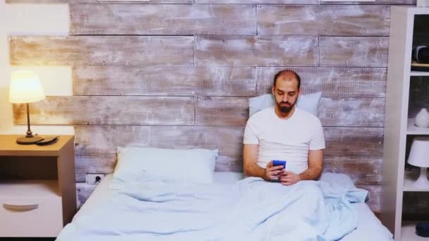 Guy browsing di smartphone di tempat tidurnya — Stok Video